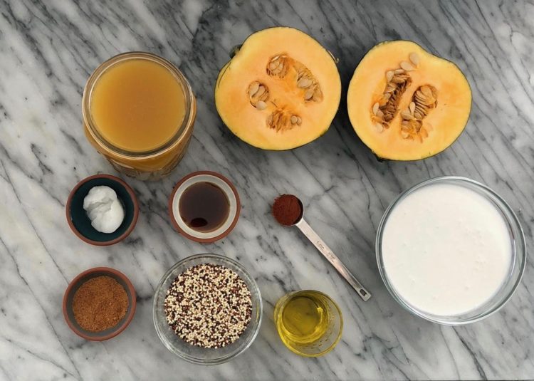 Overheat view of the ingredients needed to make acorn squash soup including acorn squash halves, vegetable stock, Thai curry paste, coconut milk, and quinoa.