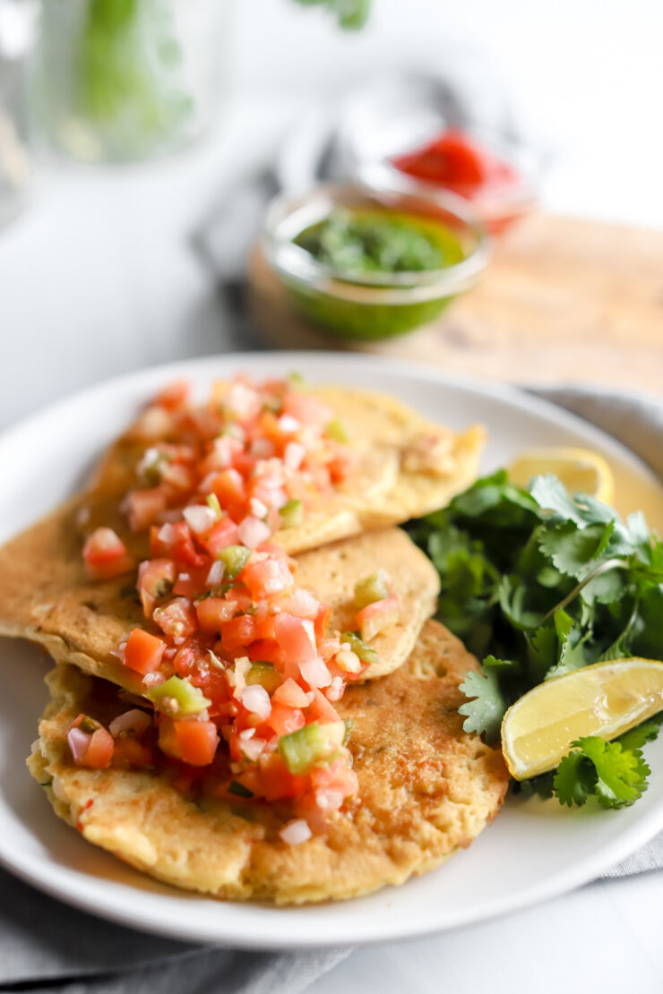 A plate of chickpea pancakes topped with salsa, lemon slices and cilantro.