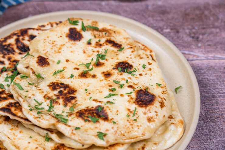 Closeup view of a pile of naan bread on a white plate with chopped cilantro sprinkled on top.