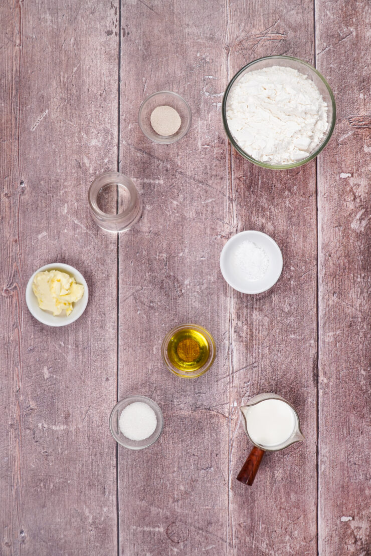 Overhead shot of bowls of ingredients needed to make Vegan Naan including yeast, sugar, soy milk, salt, bread flour, olive oil, water, and vegan butter.