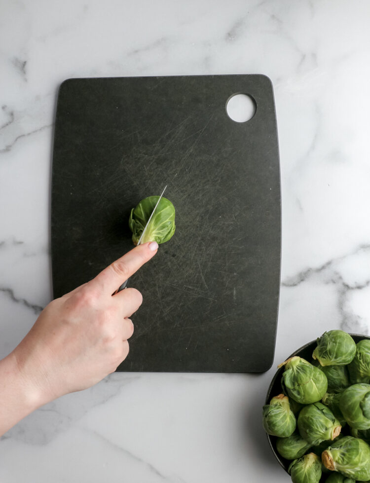 A woman chops a brussels sprout directly in half on a black chopping board.