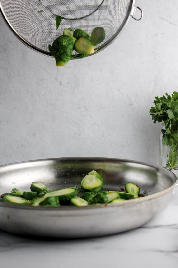 Chopped brussels sprouts are being poured out of a colander into a metal dish.