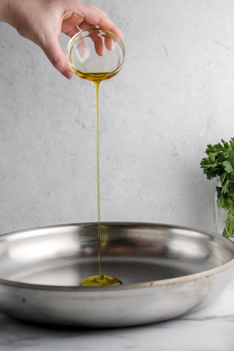 A hand pours olive oil into a metal dish.