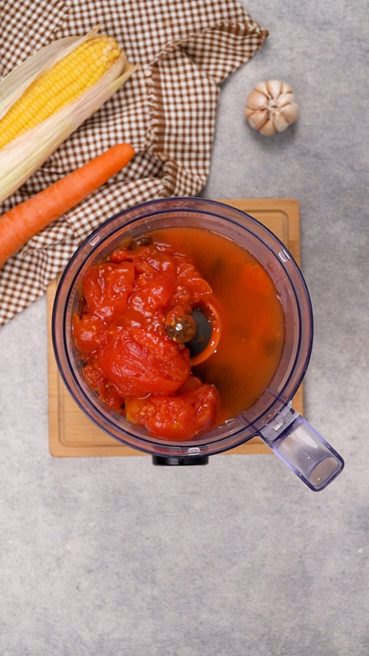Black beans, crushed tomatoes, and broth being blended in a food processor for black bean soup.