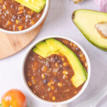 A bowl containing a black bean and corn soup recipe topped with sliced avocado.