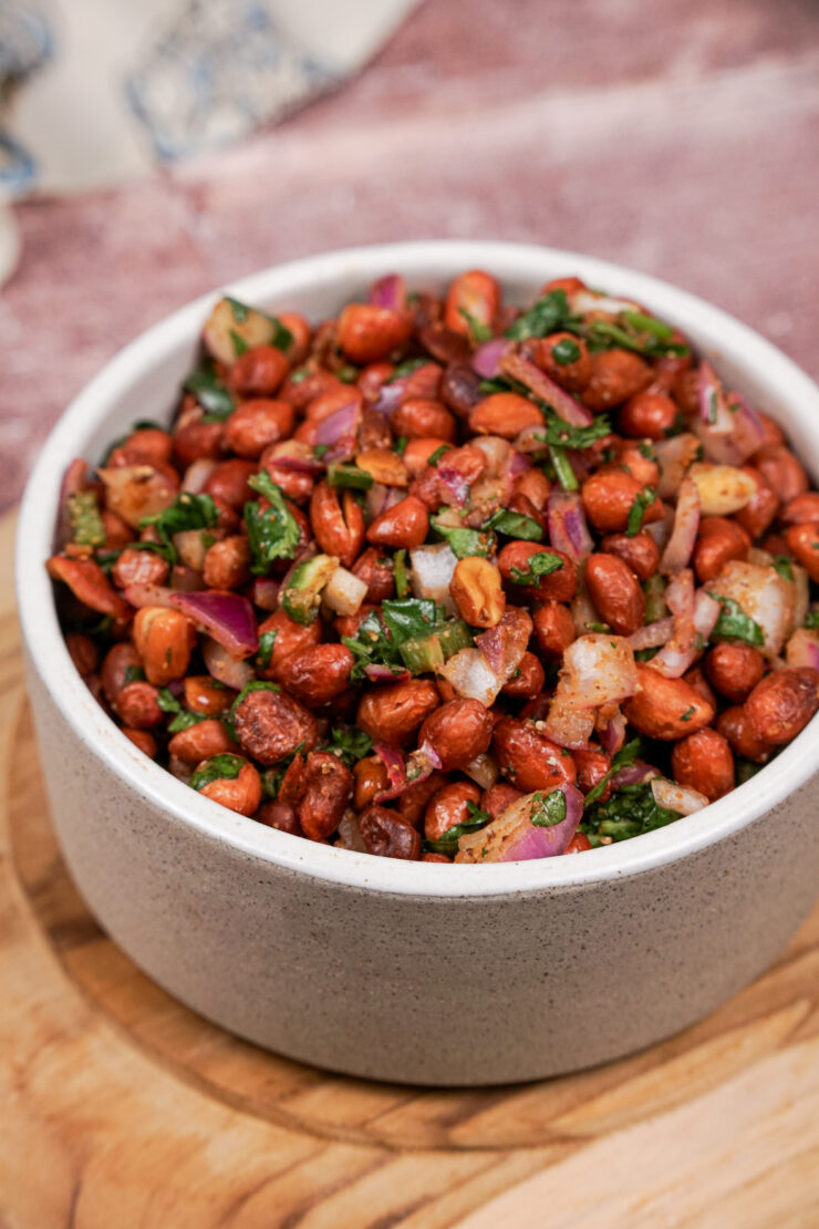 Grayish-white bowl filled with spicy cocktail peanuts mixed with sauteed red onions, jalapenos, and chopped cilantro.
