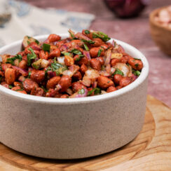 Grayish-white bowl filled with spicy cocktail peanuts with flecks of cilantro, jalapeno, and diced onion through them.