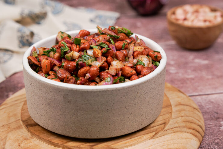 Grayish-white bowl filled with spicy cocktail peanuts with flecks of cilantro, jalapeno, and diced onion through them.