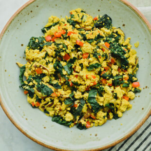 Bowl of curried tofu scramble with chopped wilted kale, mushrooms, and diced bell peppers