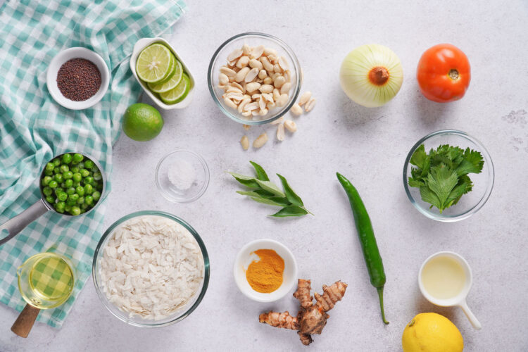 Ingredients to make poha, including peanuts, green peas, flattened rice, ginger, tomato, onion and lime.