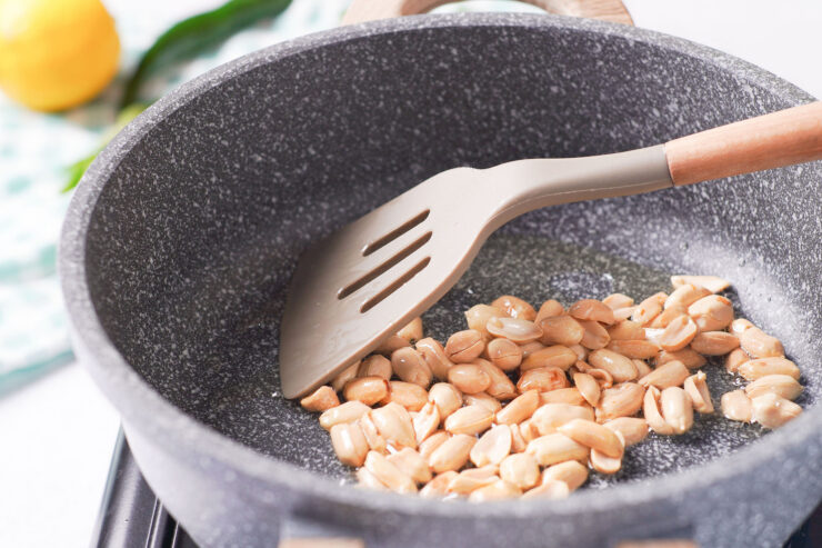 Peanuts being cooked in a skillet with olive oil until golden brown.