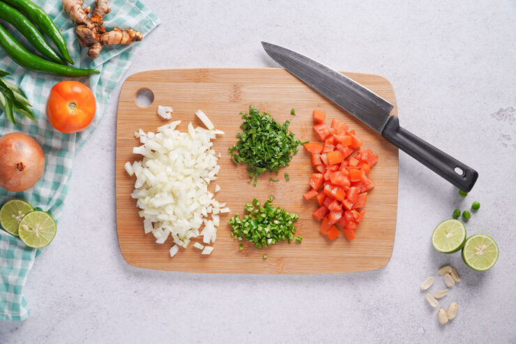 A chopping board with ingredients for poha including chopped onions, tomatoes, cilantro and green chili.