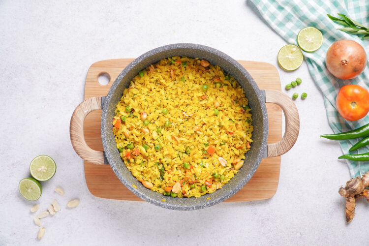 Pooha recipe with turmeric, served in a large pot and surrounded by ingredients like tomatoes and lime slices.