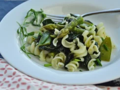 White bowl full of fusilli pasta noodles, asparagus, peas, and kale
