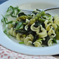 White bowl full of fusilli pasta noodles, asparagus, peas, and kale