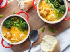 Two bowls of broccoli and carrot soup with bread on a wooden board.