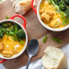 Two bowls of broccoli and carrot soup with bread on a wooden board.