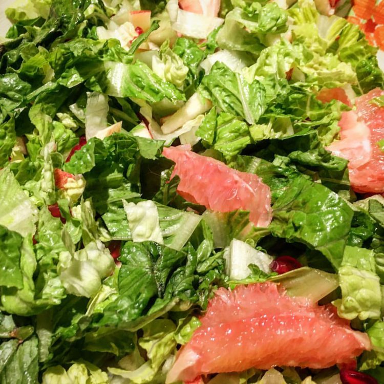 Close up of a romaine salad tossed with grapefruit segments, diced apple, and pomegranate arils