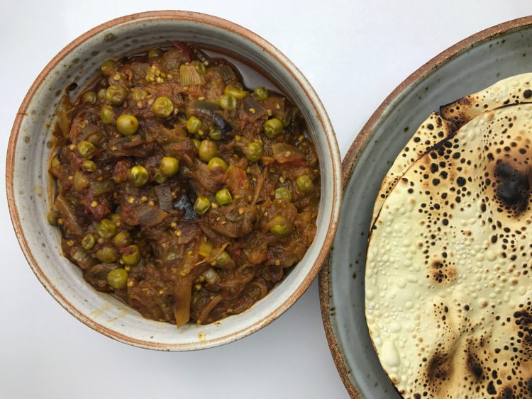 Bowl of roasted eggplant dip with a plate of flatbread on the side.