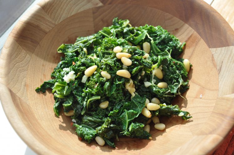Wilted kale in a wooden bowl with pine nuts