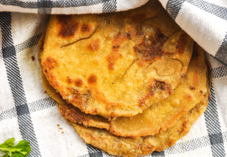 Stack of golden aloo parathas on a black and white plaid kitchen towel