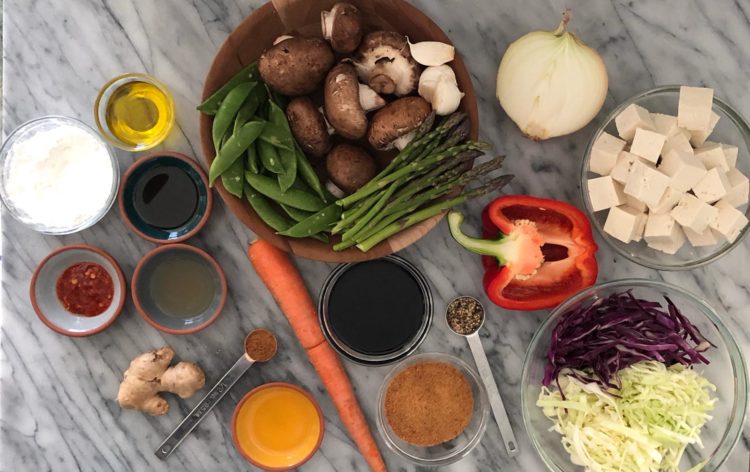 Table filled with bowls of vegetables and sauce ingredients for Szechuan Tofu Stir-fry