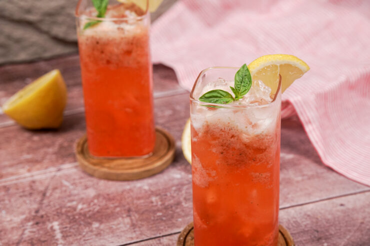 Two tall glasses filled with pink strawberry mocktail with basil and ice cubes sitting on top and lemon slices on the rims.