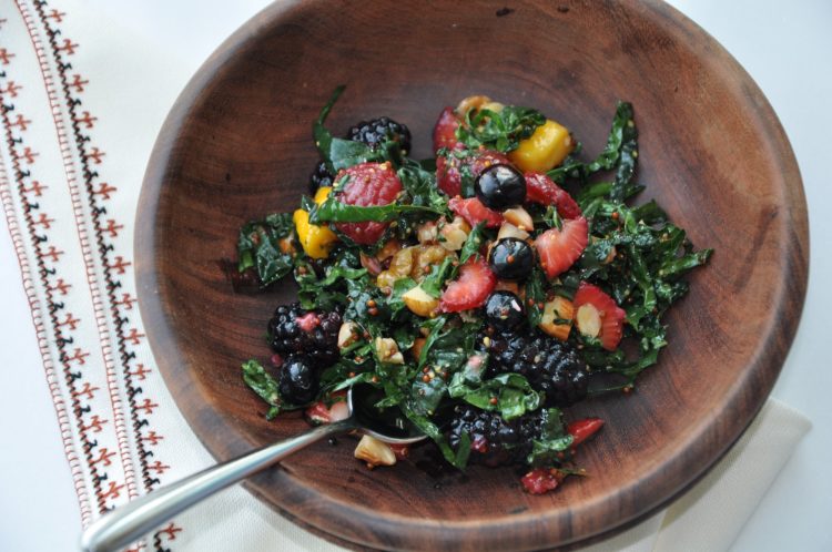 Wooden bowl full of kale salad with strawberries, blackberries, mango, almonds, and walnuts
