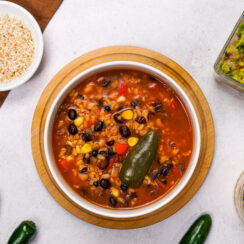 Mexican soup recipe with black beans is plated on a white countertop.