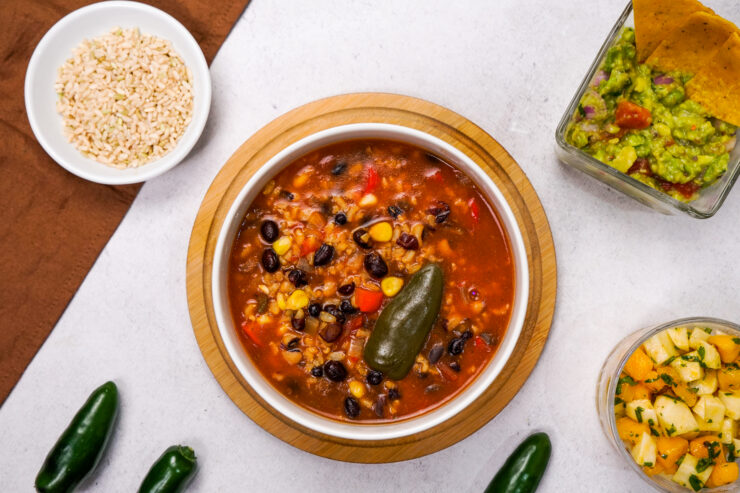 Mexican soup recipe with black beans is plated on a white countertop.