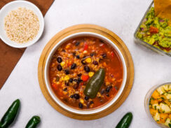Mexican soup recipe with black beans is plated on a white countertop.