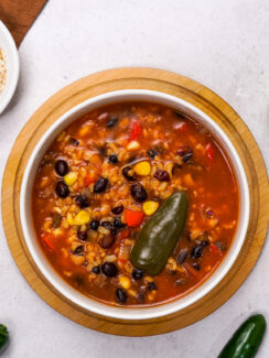 Mexican soup recipe with black beans is plated on a white countertop.