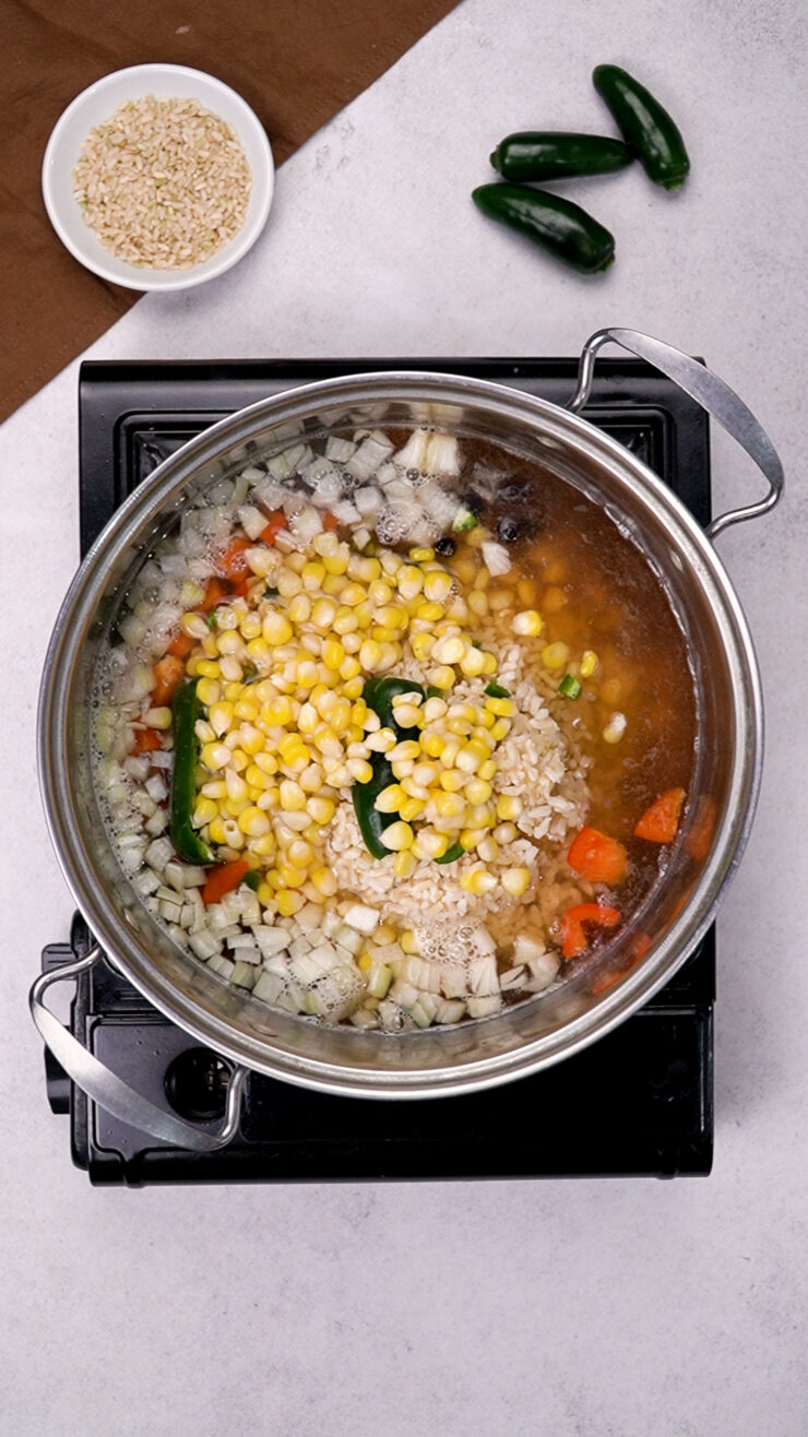 Ingredients for Mexican soup simmer in a pot, including onion, corn and garlic.