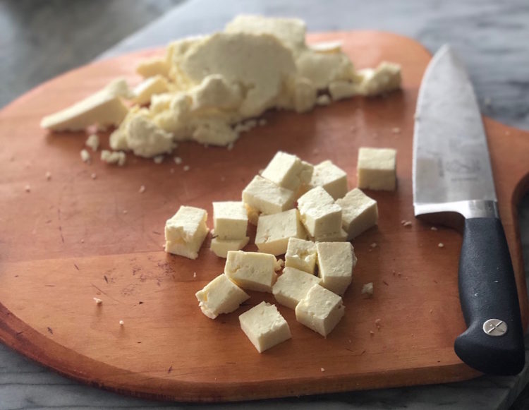 Wooden board with a knife and a pile of cubed paneer cheese