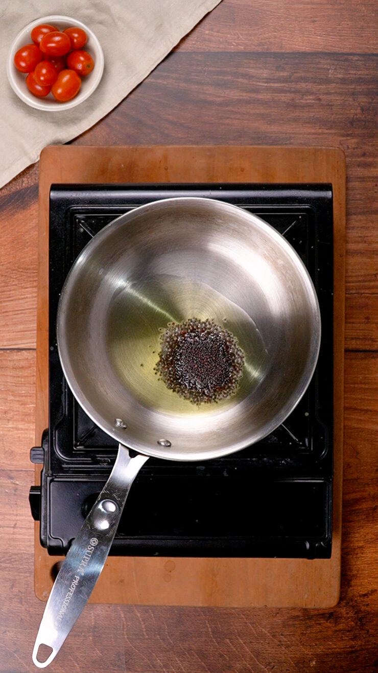 A stovetop pot with hot oil and mustard seeds, making a mustard seeds tadka.