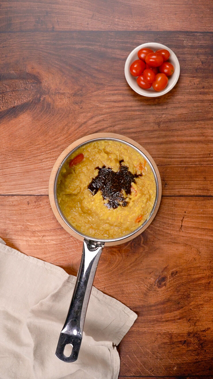 A pot of South Indian dal topped with mustard seed tadka, next to a bowl of tomatoes.