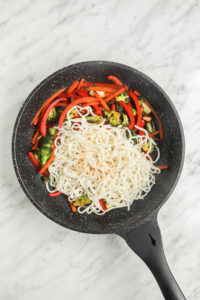 Ramen in a frying pan with vegetables.
