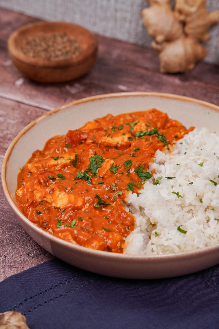 Light colored bowl with tofu tikka masala with chunks of tofu on one side and basmati rice on the other side with chopped cilantro sprinkled on top.