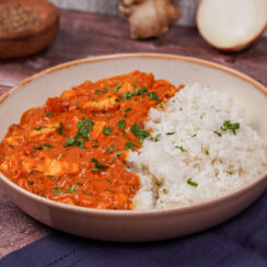 Gray bowl with red tofu tikka masala on one side and fluffy basmati rice on the other side, and a sprinkling of chopped cilantro on top.