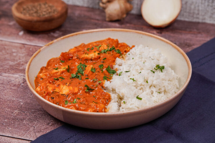 Gray bowl with red tofu tikka masala on one side and fluffy basmati rice on the other side, and a sprinkling of chopped cilantro on top.