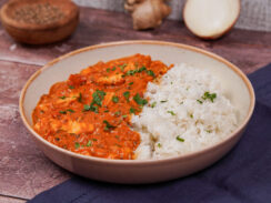 Gray bowl with red tofu tikka masala on one side and fluffy basmati rice on the other side, and a sprinkling of chopped cilantro on top.