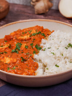 Gray bowl with red tofu tikka masala on one side and fluffy basmati rice on the other side, and a sprinkling of chopped cilantro on top.