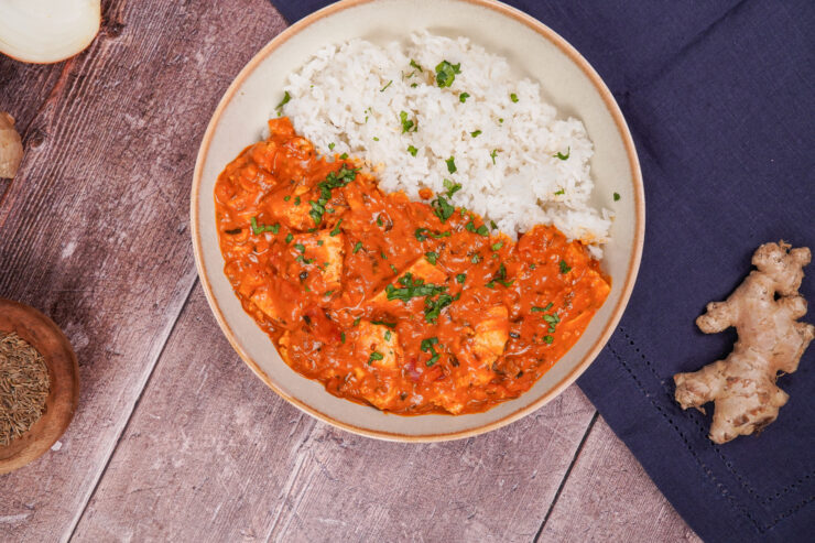 Overhead shot of a bowl filled with tofu tikka masala on one side and basmati rice on the other side. You can see the chunks of tofu in the sauce and there is cilantro sprinkled on top for garnish.