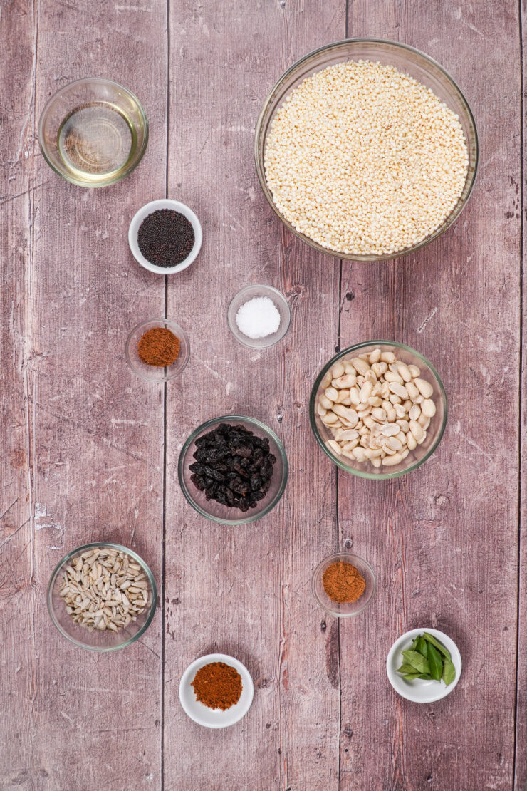 Overhead view of bowls of ingredients needed to make namkeen including puffed millet, spices, raisins, and sunflower seeds.