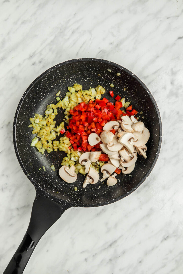 A pan containing the first ingredients for curried tofu scramble, including sliced mushrooms, chopped tomatoes and garlic.