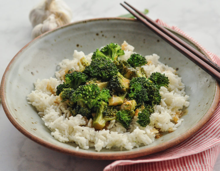 A plate of broccoli with garlic sauce served on jasmine rice, alongside chopsticks.