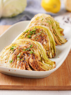 Plated oven-baked cabbage wedges coated in mustard and fresh parsley.