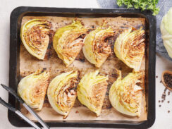 Baked cabbage wedges with mustard are arranged on brown paper on a baking tray.