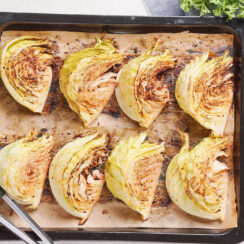 Baked cabbage wedges with mustard are arranged on brown paper on a baking tray.