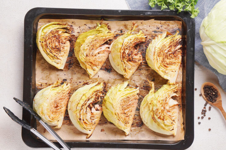 Baked cabbage wedges with mustard are arranged on brown paper on a baking tray.